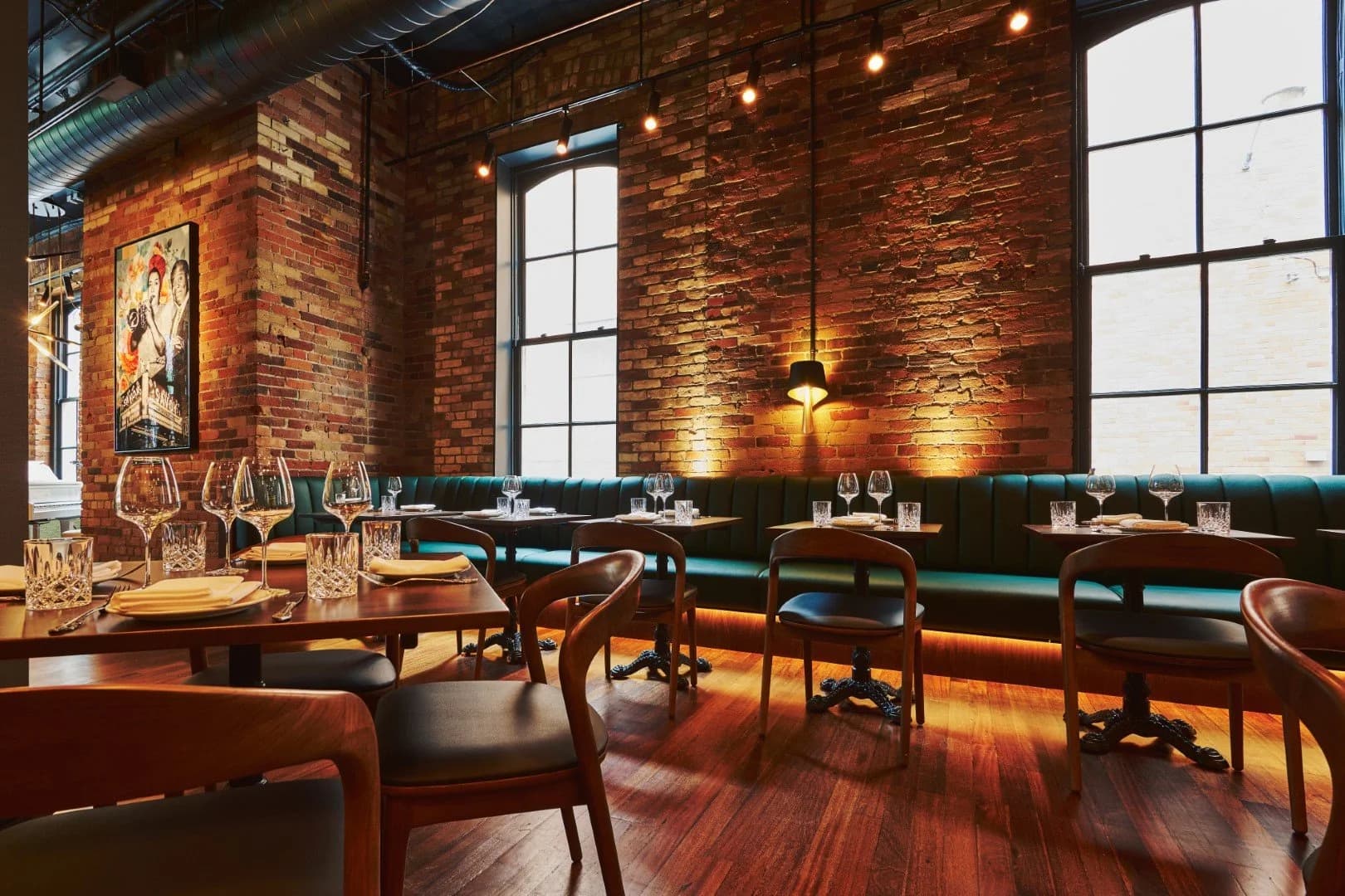 Heritage brick dining room with green banquette seating and tall windows at The Berczy Tavern