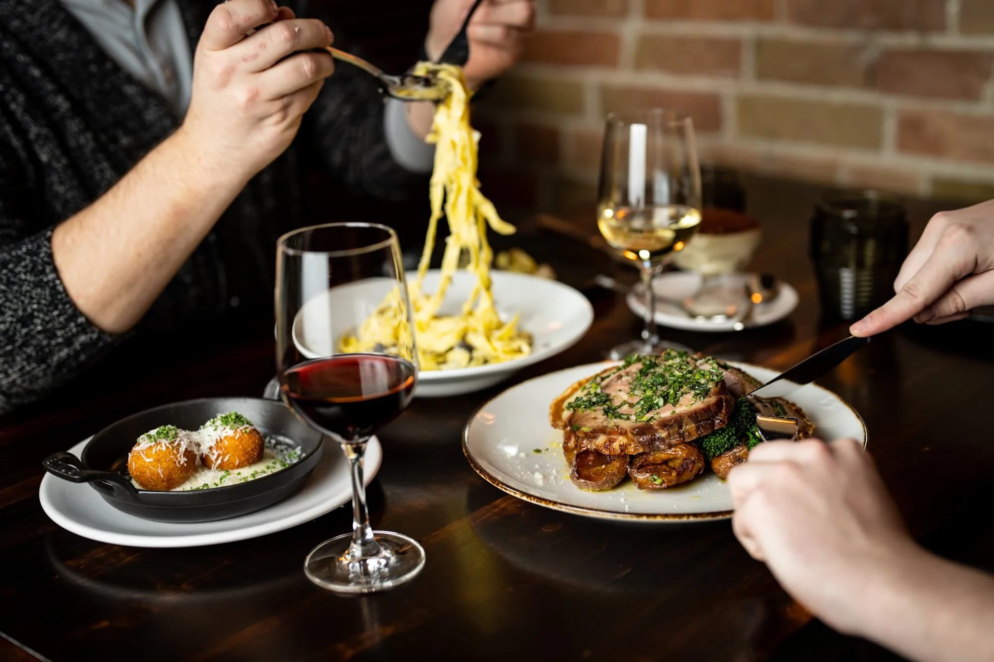 Shared dinner table with pasta, a meat main, arancini, and wine at The Berczy Tavern